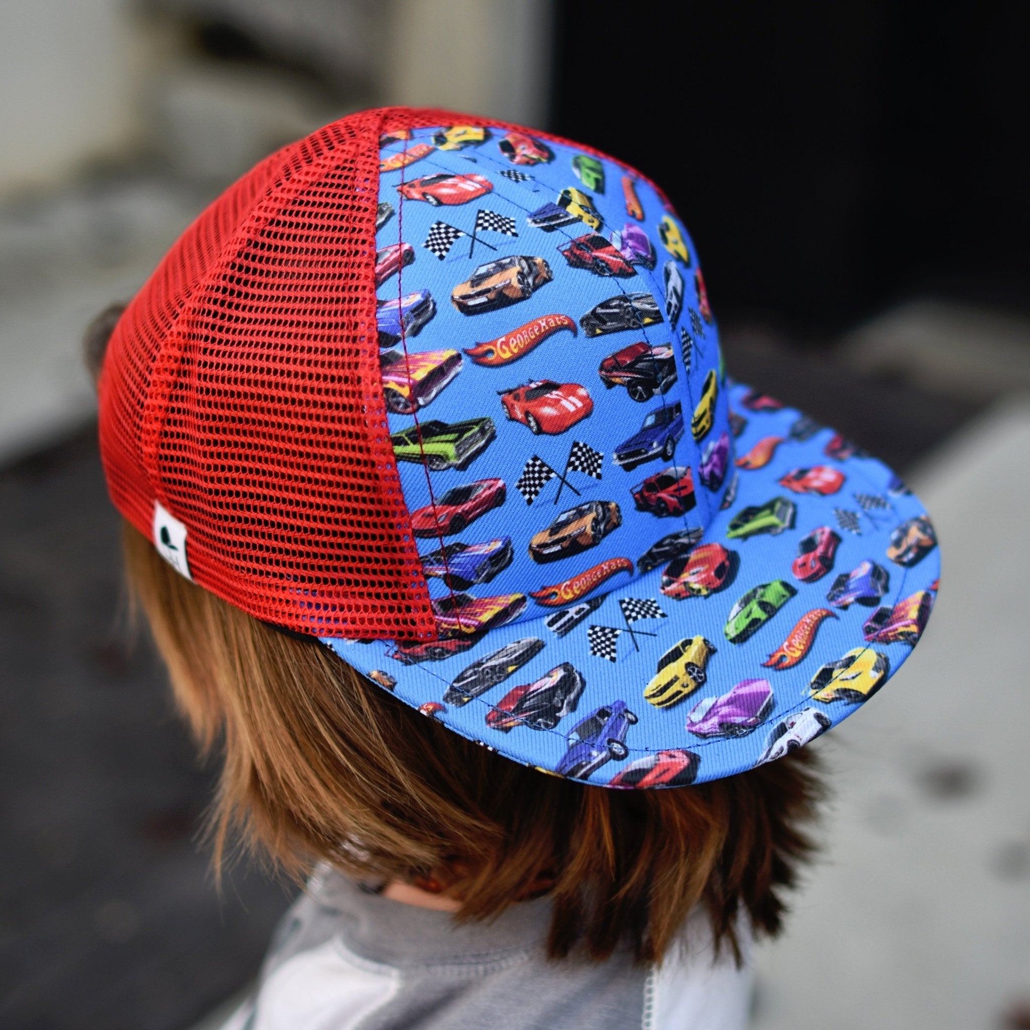 Image of a boy in a blue and red hat with cars on the front and brim - Hot Wheels Trucker - George Hats