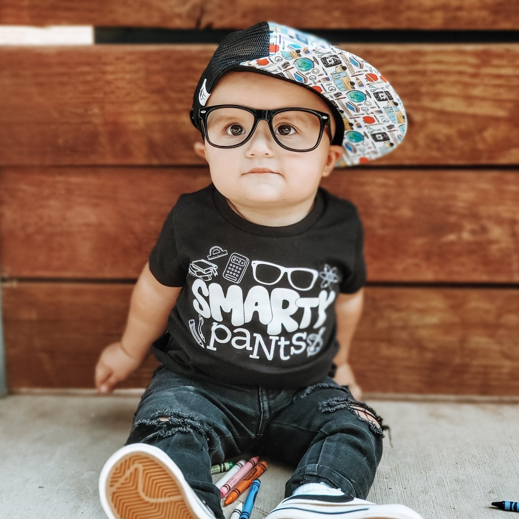 image of a baby wearing oversized glasses, a tshirt reading 'smarty pants' and the Back to School Trucker - George Hats, a boys trucker hat with school themed print