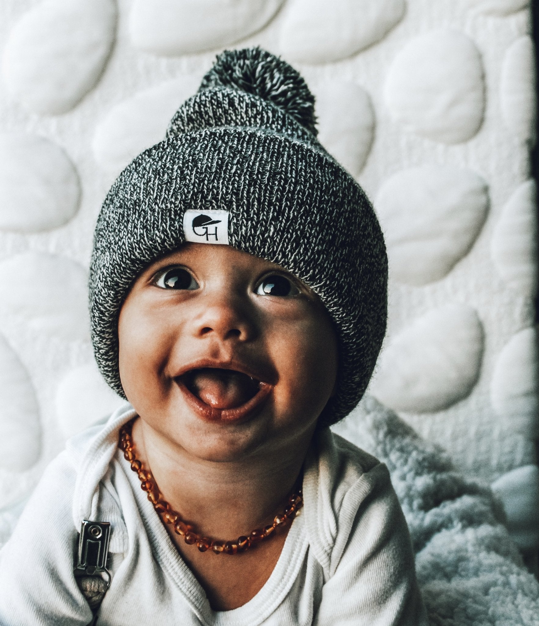 image of smiling toddler looking up towards the camera wearing the Black Marled Pom Beanie - George Hats baby beanie hat