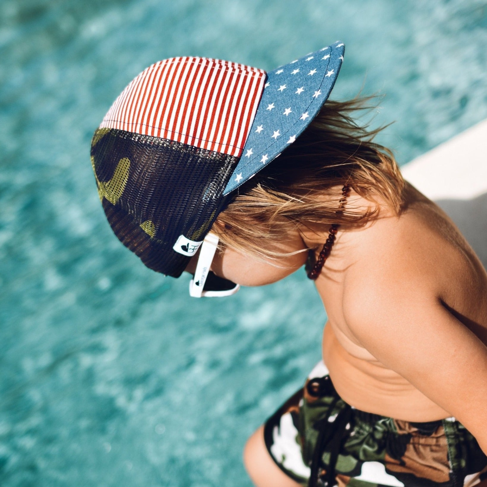 An image of a child in the Camo Patriotic Trucker. 