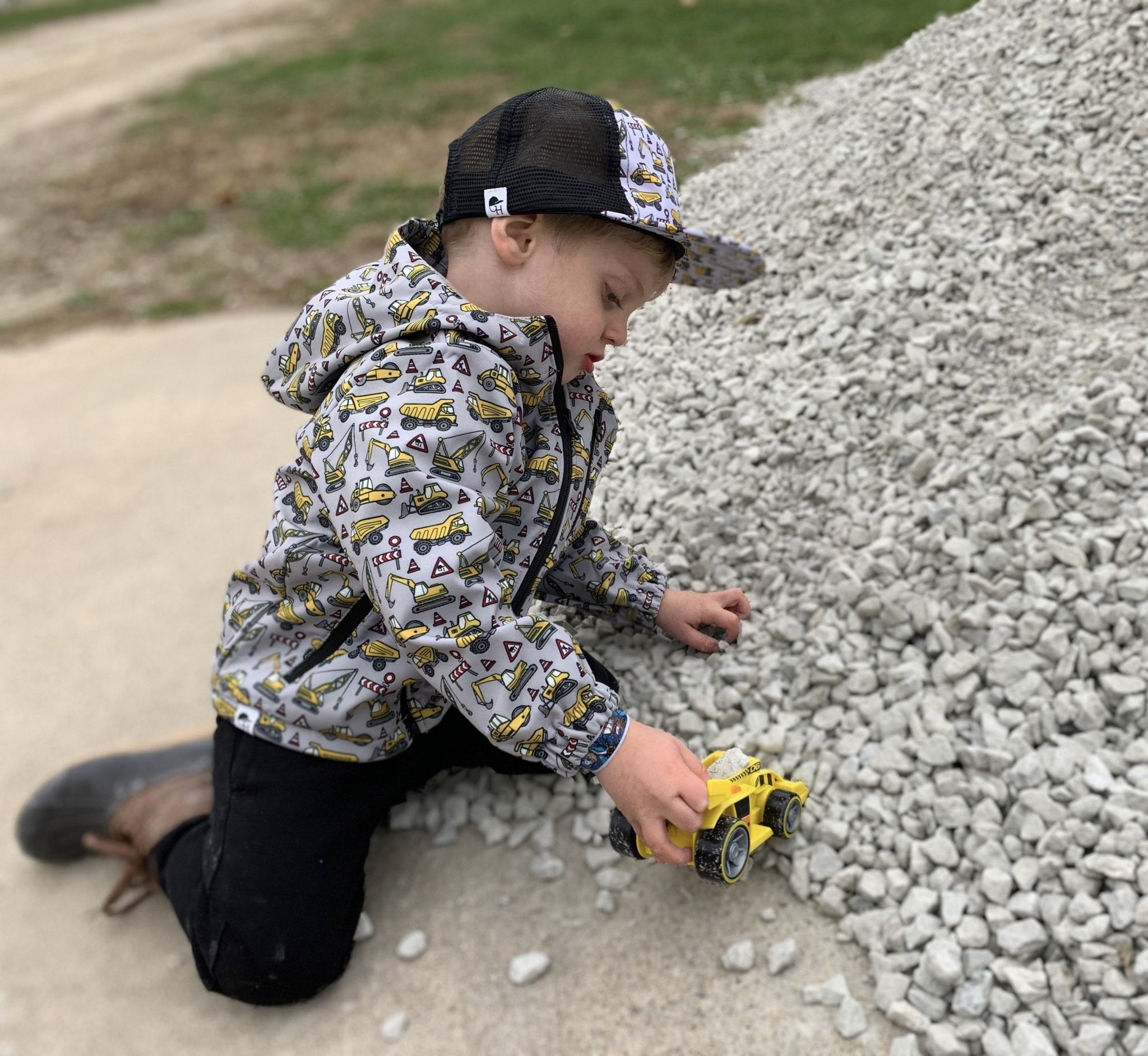 Image a toddler wearing the Construction Jacket from George Hats and playing with a truck next to a pile of rocks