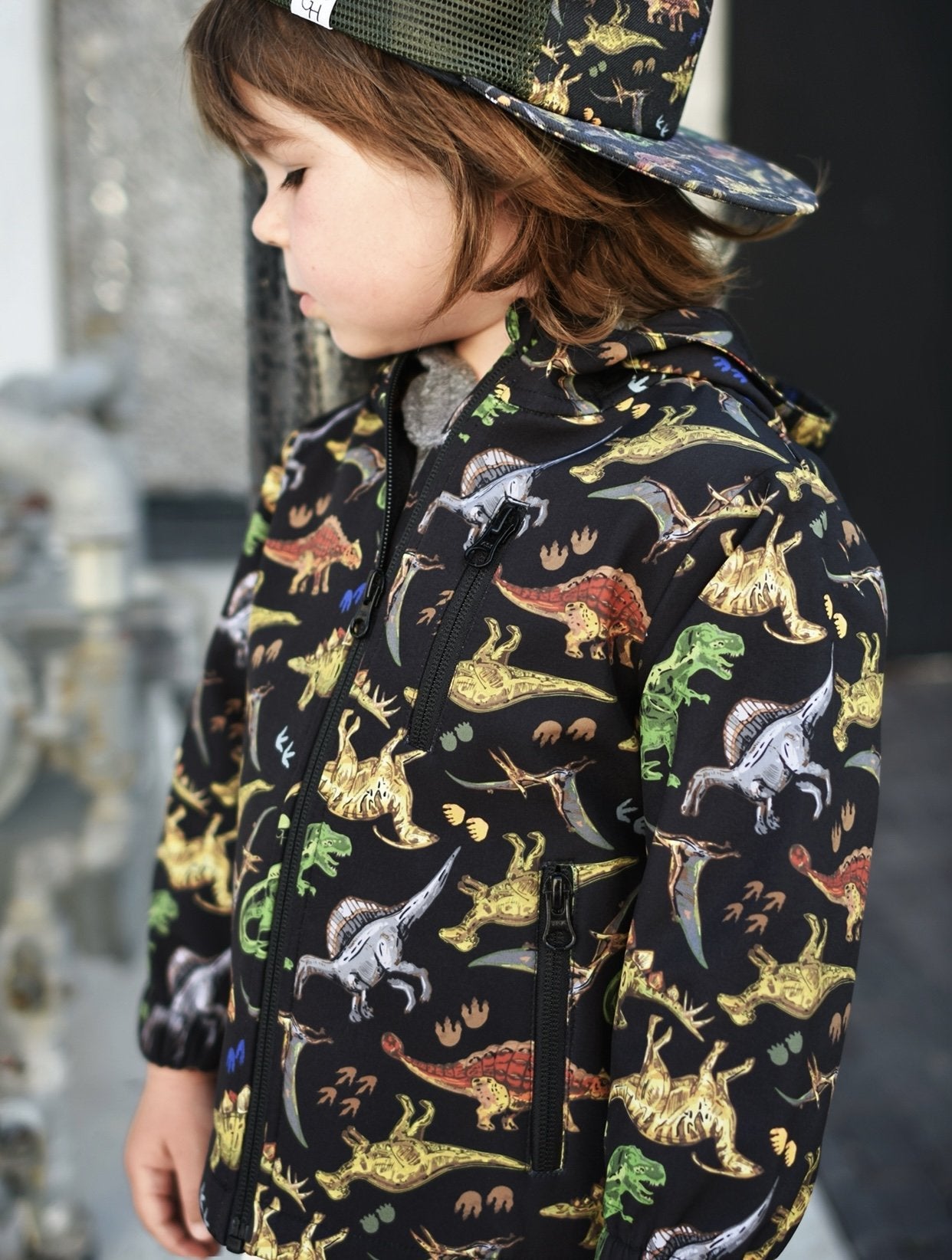 image of a toddler looking away from the camera wearing the Dinosaur Jacket - George Hats little boys winter coats