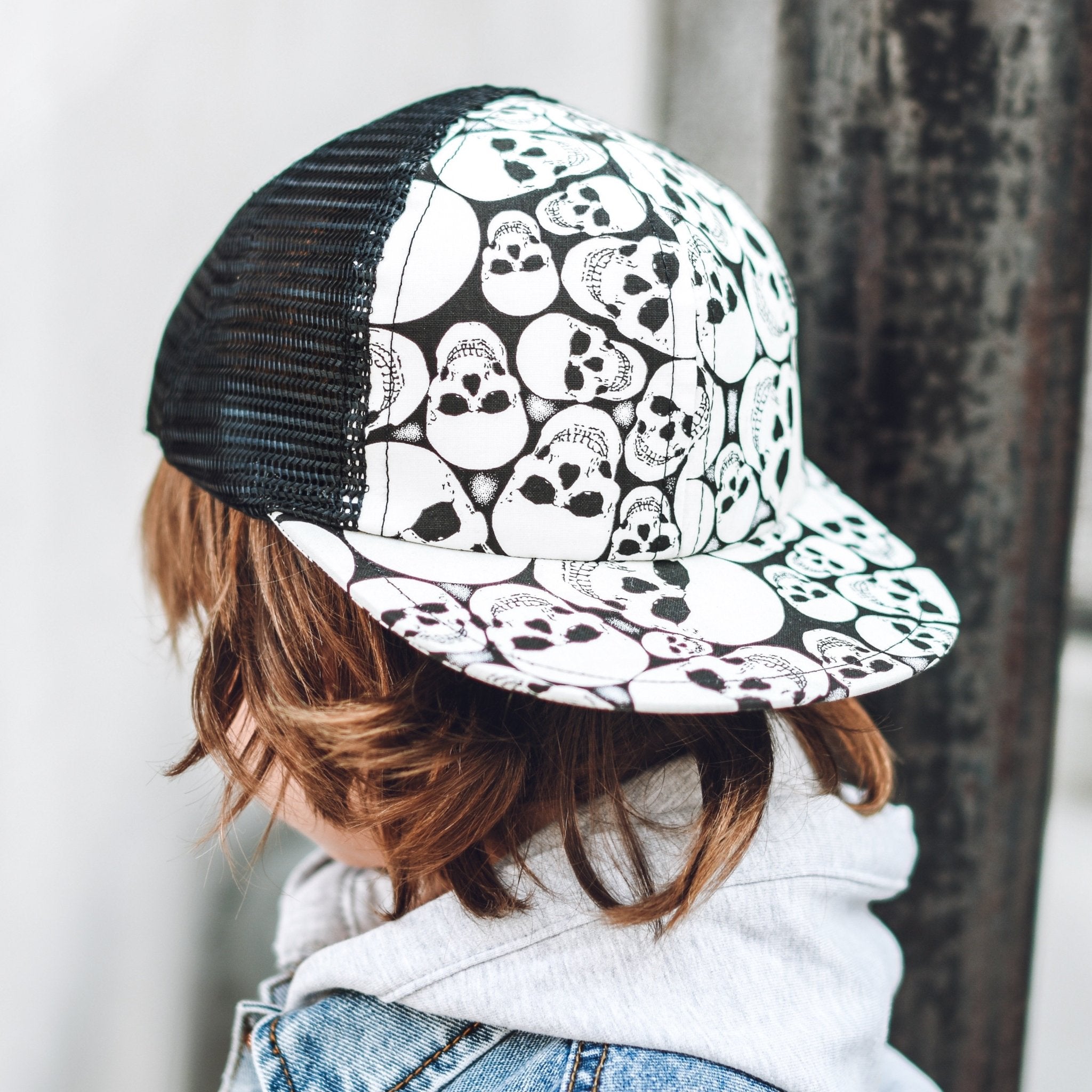 Closeup image of a boy in a kid's trucker hat with black and white skull print -Glow Skulls Trucker - George Hats