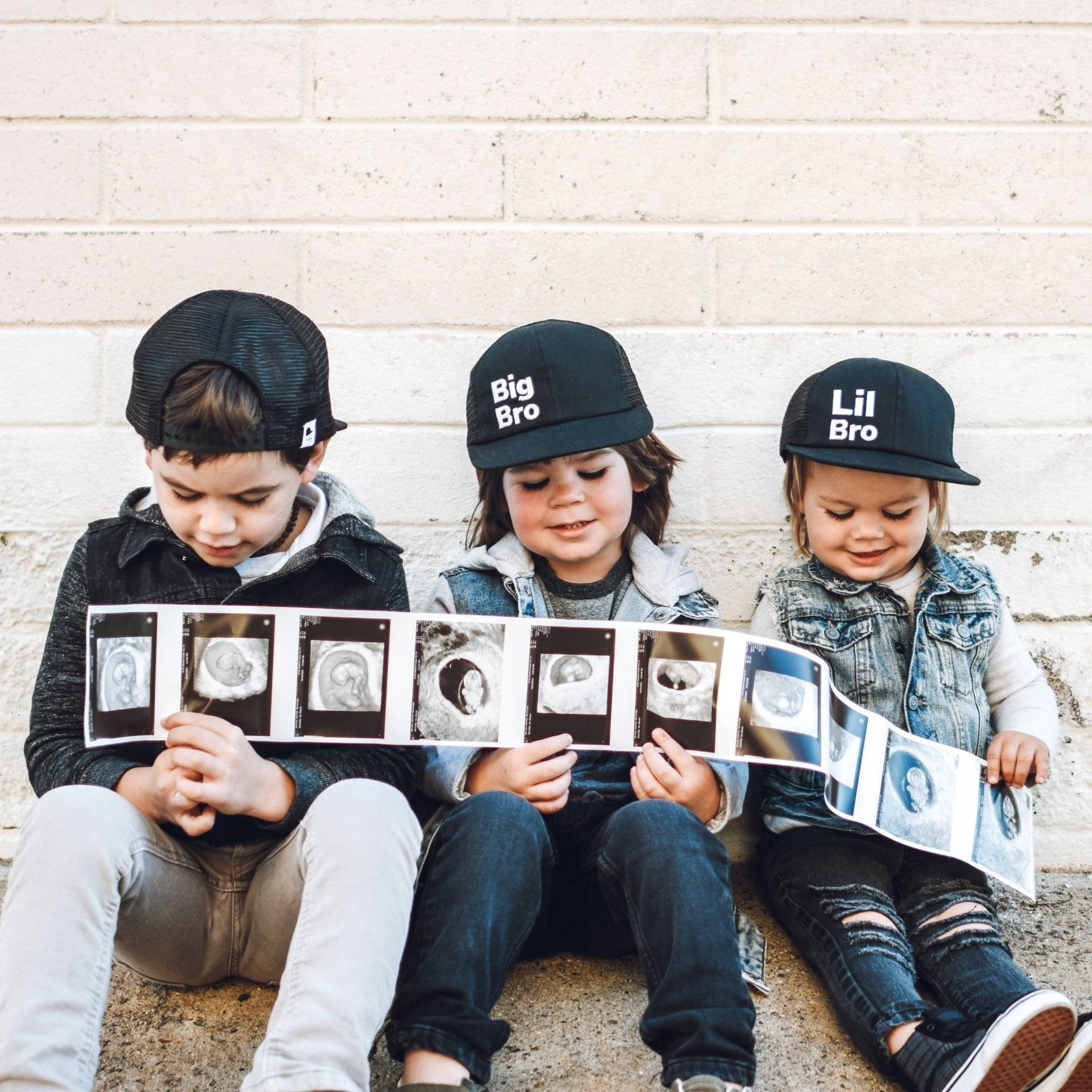 Picture of three boys in lil bro trucker and big boy trucker hats holding an ultrasound image