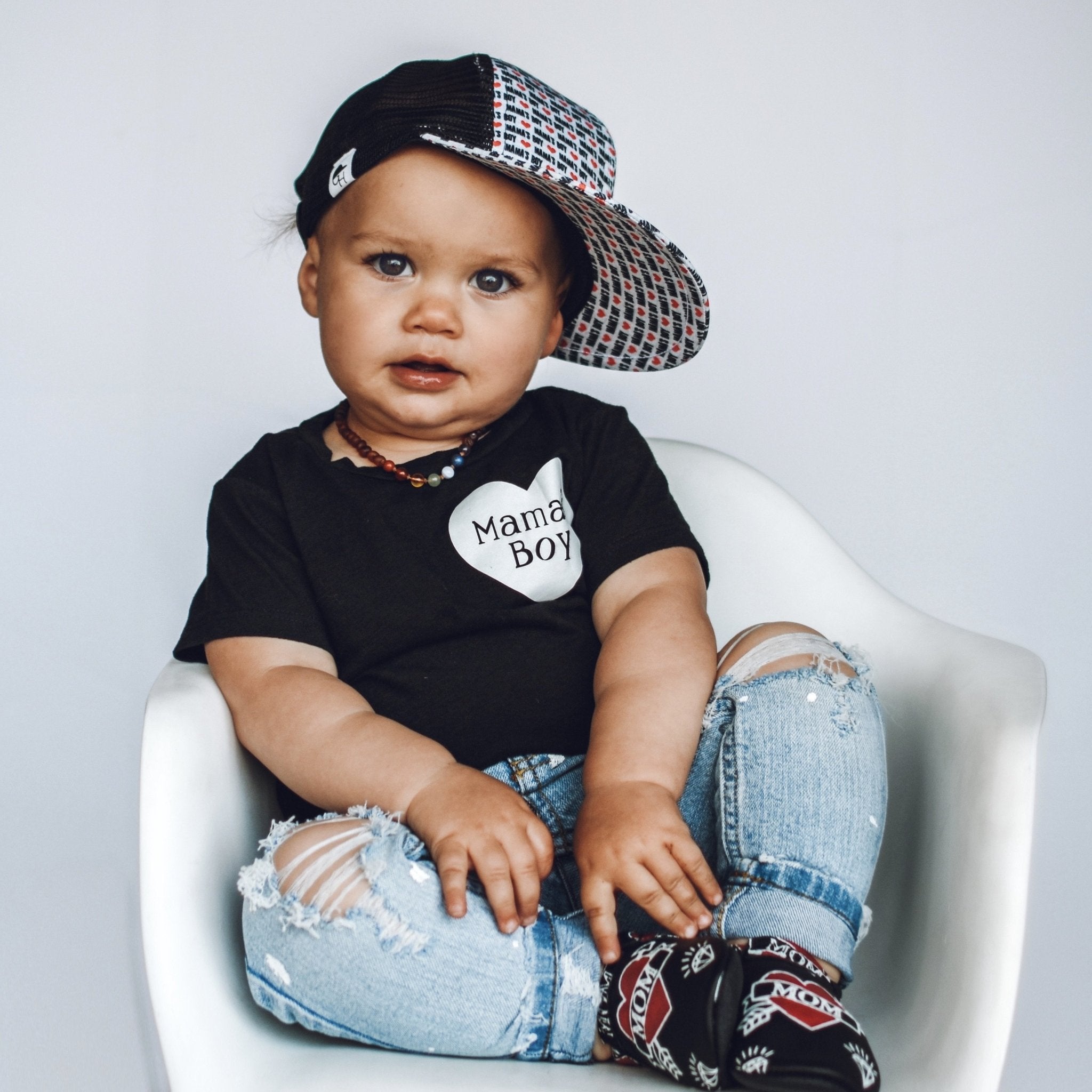 Image of a boy wearing a boy trucker hat with the words “mama’s boy” printed on the hat with red hearts