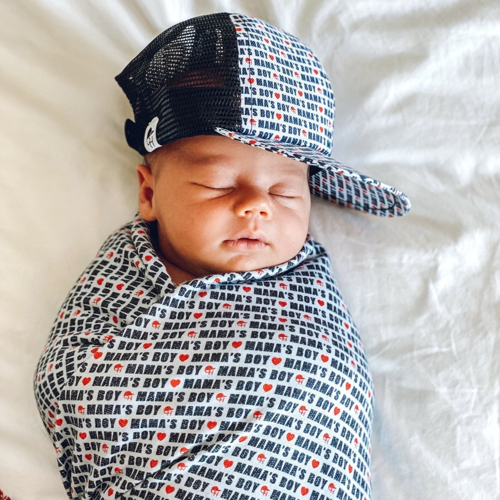 Image of an infant wearing a kids trucker hat from George Hats with “mama’s boy” printed on the hat