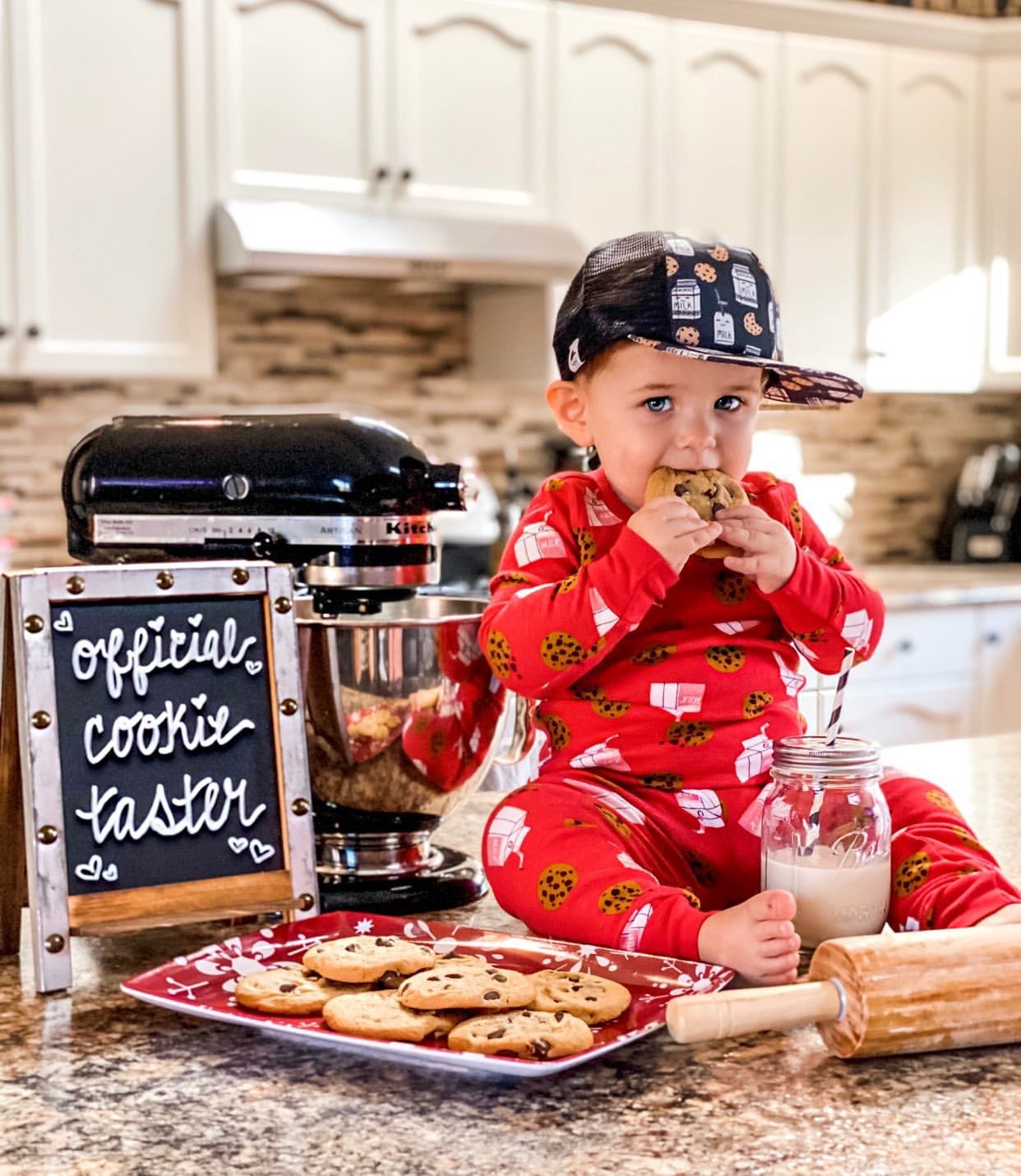 Image of a toddler sitting the counter in red pajamas and the Milk and Cookies kids trucker hat from George hats and eating milk and cookies