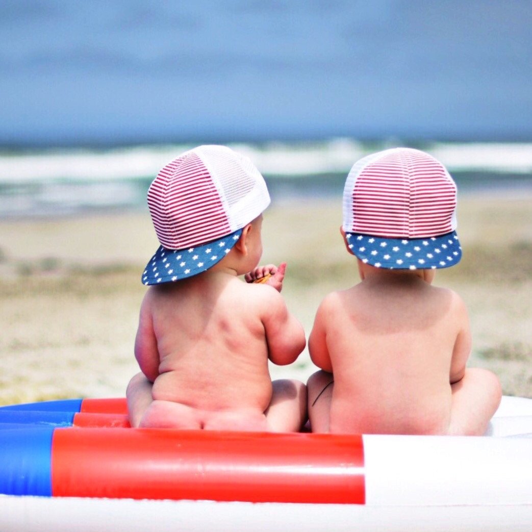 Image of two children in a trucker hat on the beach.