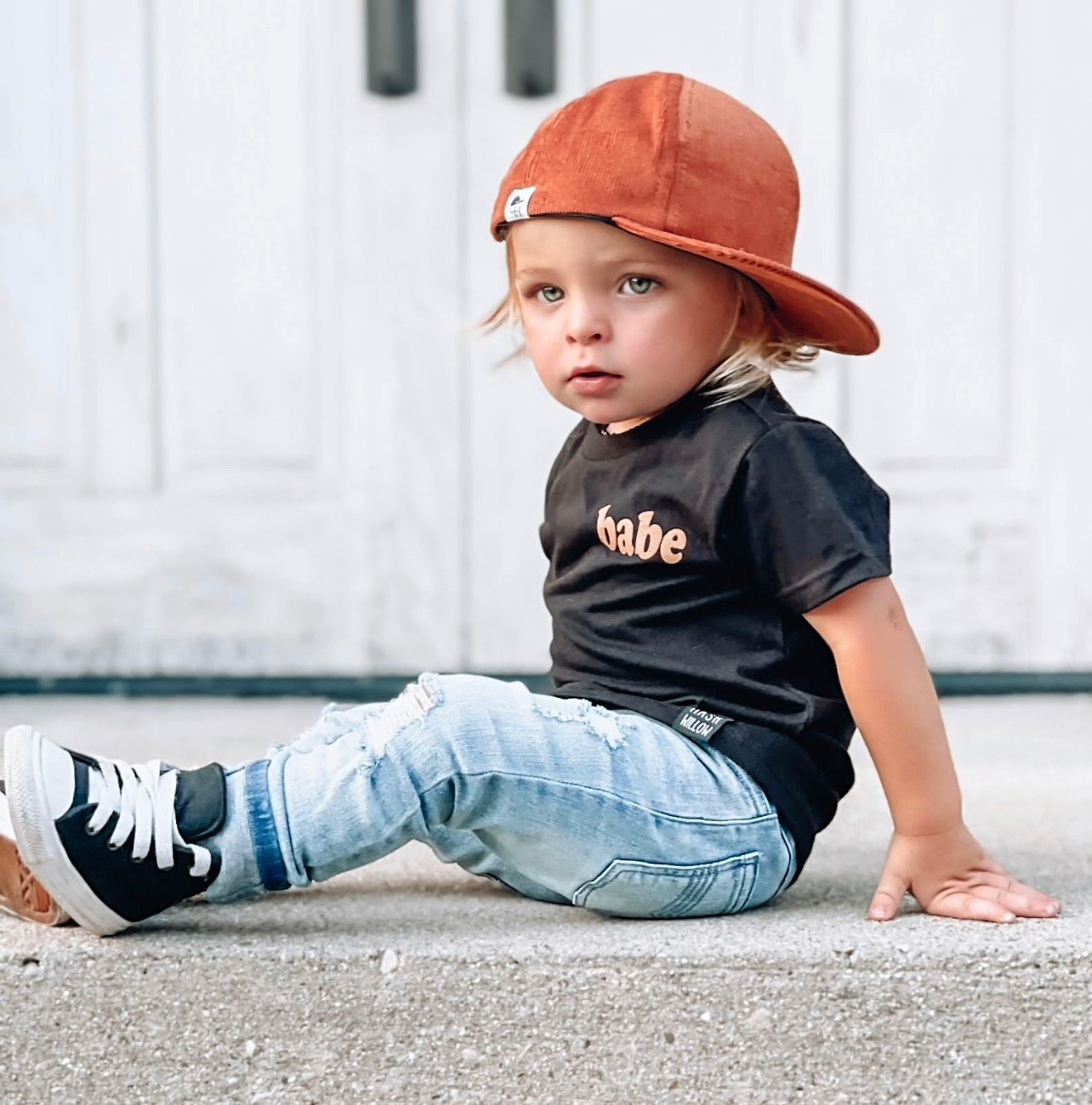 image of a toddler sitting on a concrete stoop wearing the Pumpkin Corduroy Trucker - George Hats boys trucker hat