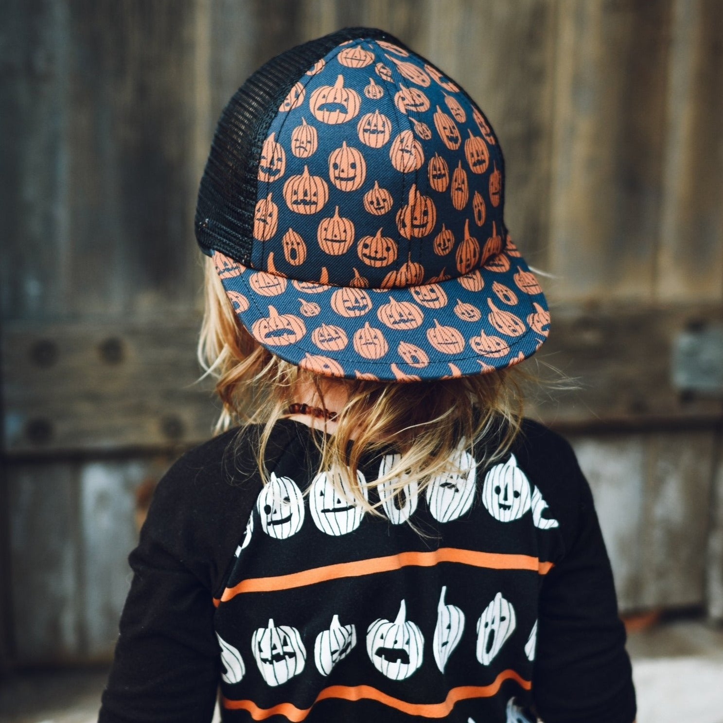 image of a baby looking away from the camera wearing the Pumpkin Trucker Rags Collab - George Hats with a pumpkin print