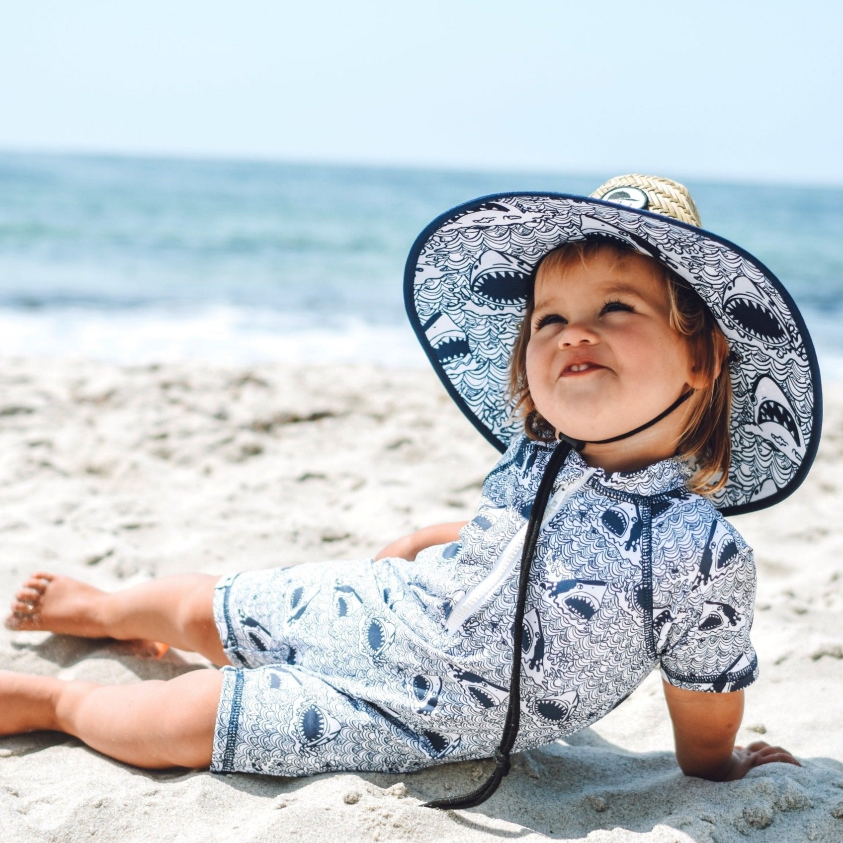 An image of a child on the beach in the Shark Straw Hat and Sunsuit.