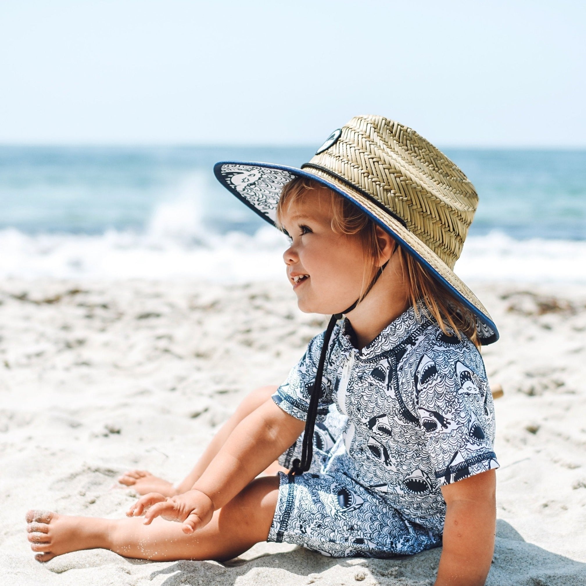 An image of a child on the beach in the Shark Straw Hat and Sunsuit.